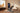 Man using a digital home strength-training machine to pull an overhead bar in a sunlit living room
