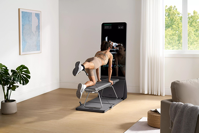Person doing a dumbbell workout on a foldable weight bench in front of a smart mirror.