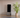 A sleek smart home gym station stands against a wall next to a potted palm, positioned in front of a workout mat for a high-tech fitness session.