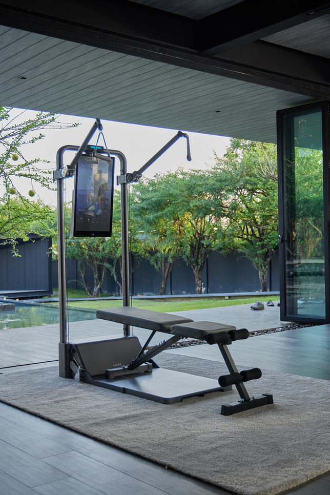 Digital cable strength-training station with a touchscreen, adjustable arms, and a padded bench in a bright home gym.
