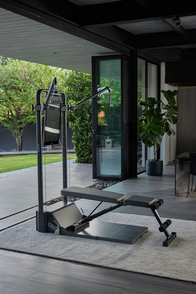 Cable exercise station with adjustable pulleys, a workout bench, and a foot platform in a bright home gym.
