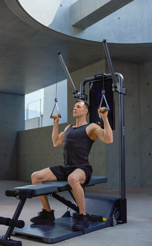 Man seated at a cable machine, pulling two overhead handles down toward his shoulders
