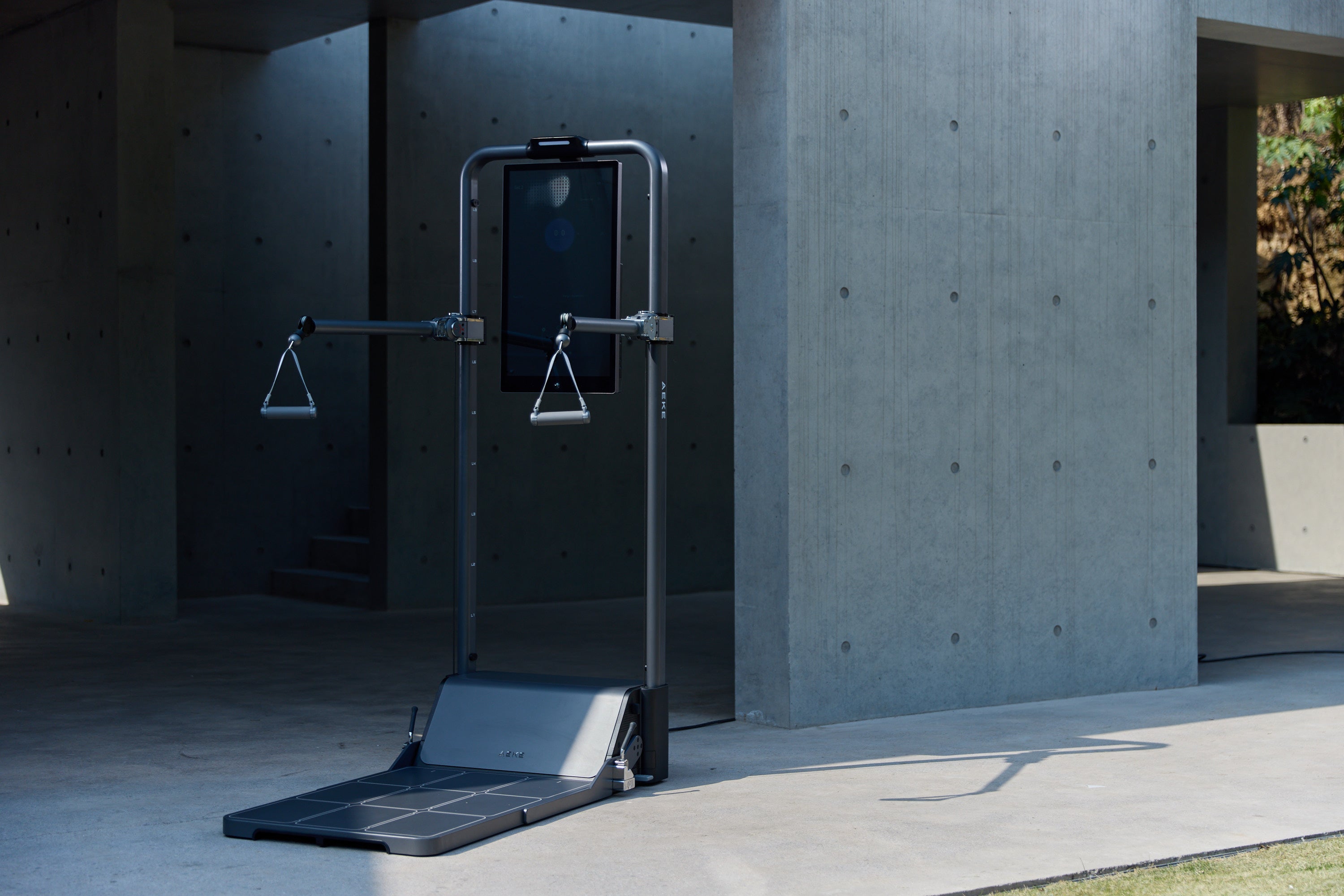 Freestanding digital cable-training machine with a touchscreen, adjustable pulley arms, hanging handles, and a foot platform